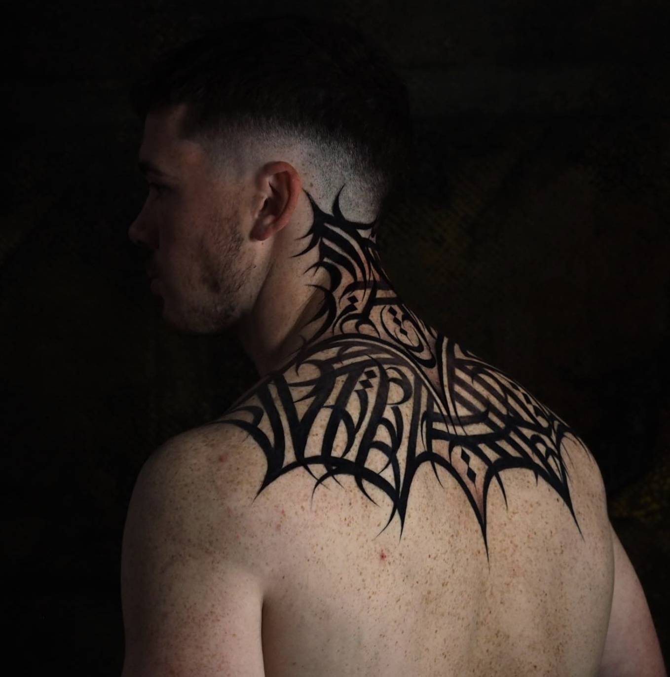 Side view of man's neck and upper back with bold abstract tribal tattoo pattern